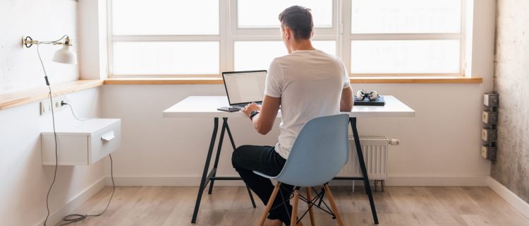 young handsome man in casual outfit sitting at table working on laptop, freelancer at home, view from back